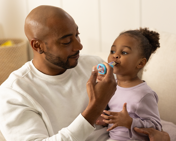 Man holding a child as they use a rocket ship medicine dispenser together.